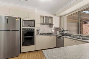 A modern kitchen with stainless steel appliances, a built-in oven, and a dishwasher. - The Wattle House - Your Home Away From Home (Sydney)