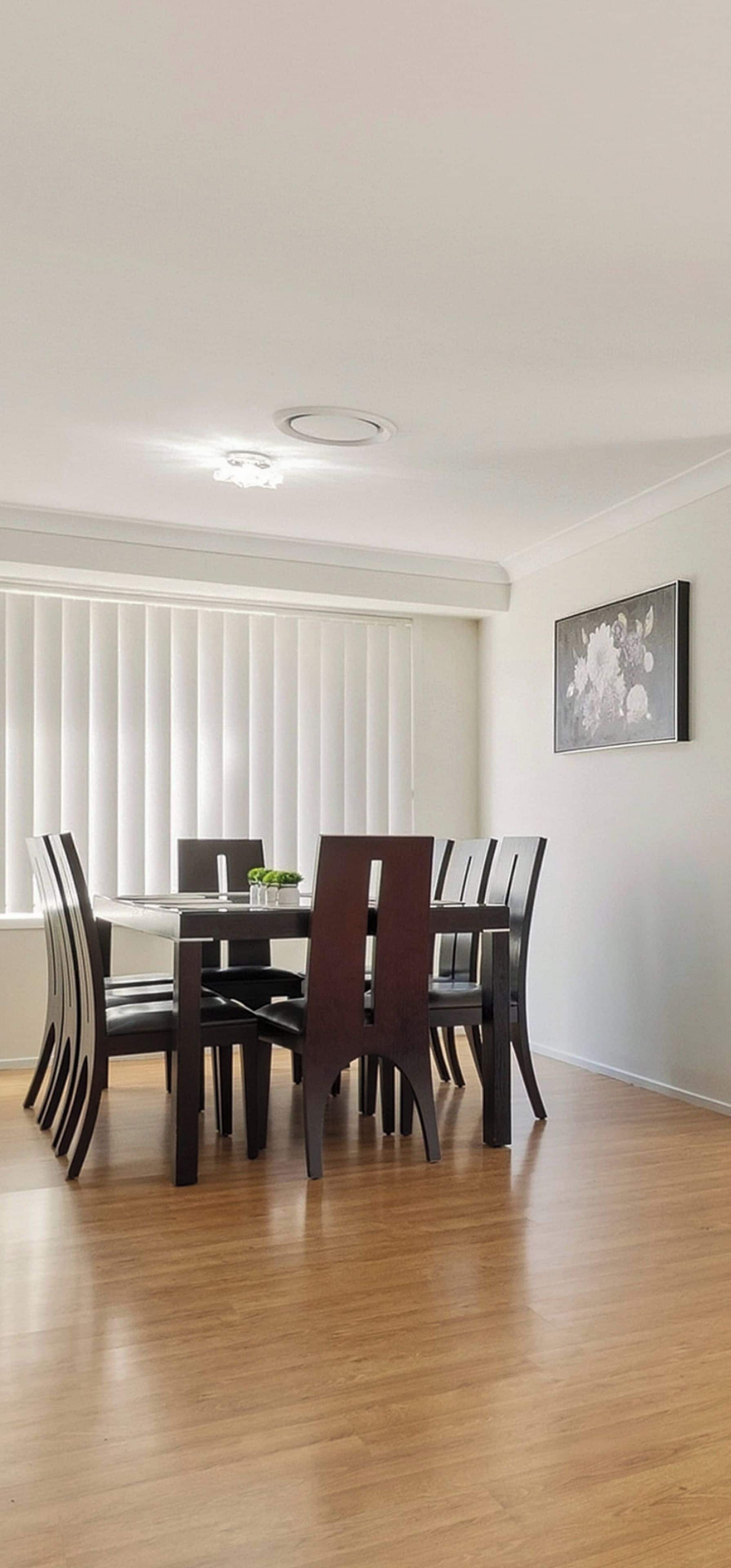 A dining area with a table and chairs, a ceiling light, a window with blinds, and a framed picture on the wall.