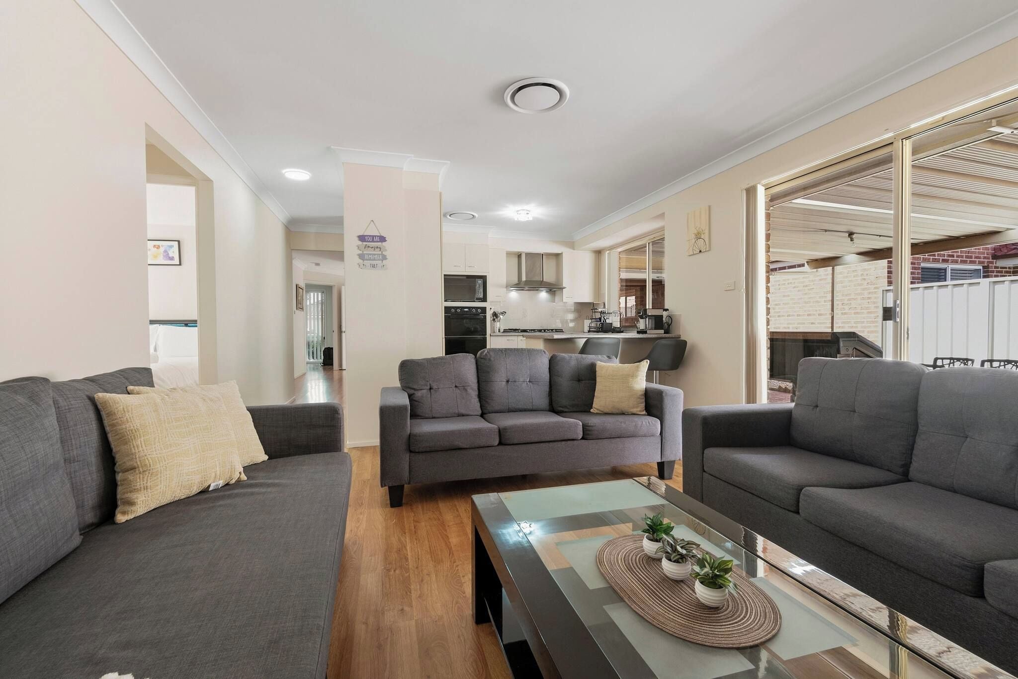 A modern living room with a sofa set, a coffee table, and a kitchen in the background.