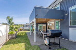 A modern outdoor patio with a grill and seating area. - Peaceful Paradise | The Family Retreat (Whitianga)
