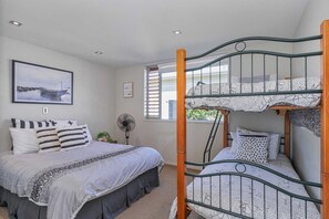 A bedroom with a bunk bed, a single bed, and a fan. There is a window with blinds, a framed picture on the wall, and a ceiling light. - Peaceful Paradise | The Family Retreat (Whitianga)