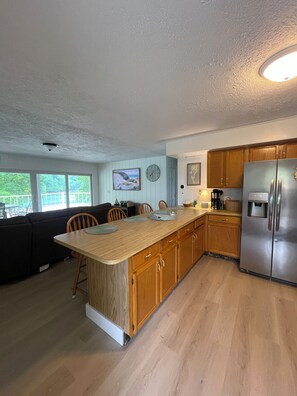 A kitchen with wooden cabinets, a stainless steel refrigerator, and a dining area with a wooden table and chairs. - Norris Lakefront Retreat — House + Cabin — Sleeps 18 (LaFollette)