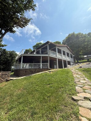 Ein zweistöckiges Haus mit Stein Fundament, einer Veranda mit weißen Geländern und einem Steinweg, der zum Eingang führt.