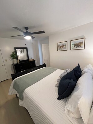 Ein Schlafzimmer mit einem Bett, einem Deckenventilator, einer Kommode, einem Spiegel und zwei gerahmten Bildern an der Wand.