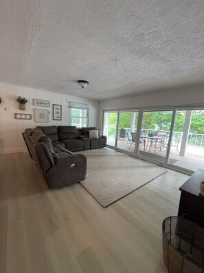 A modern living room with a sectional sofa, a large window, and a view of the outdoors. - Norris Lakefront Retreat — House + Cabin — Sleeps 18 (LaFollette)