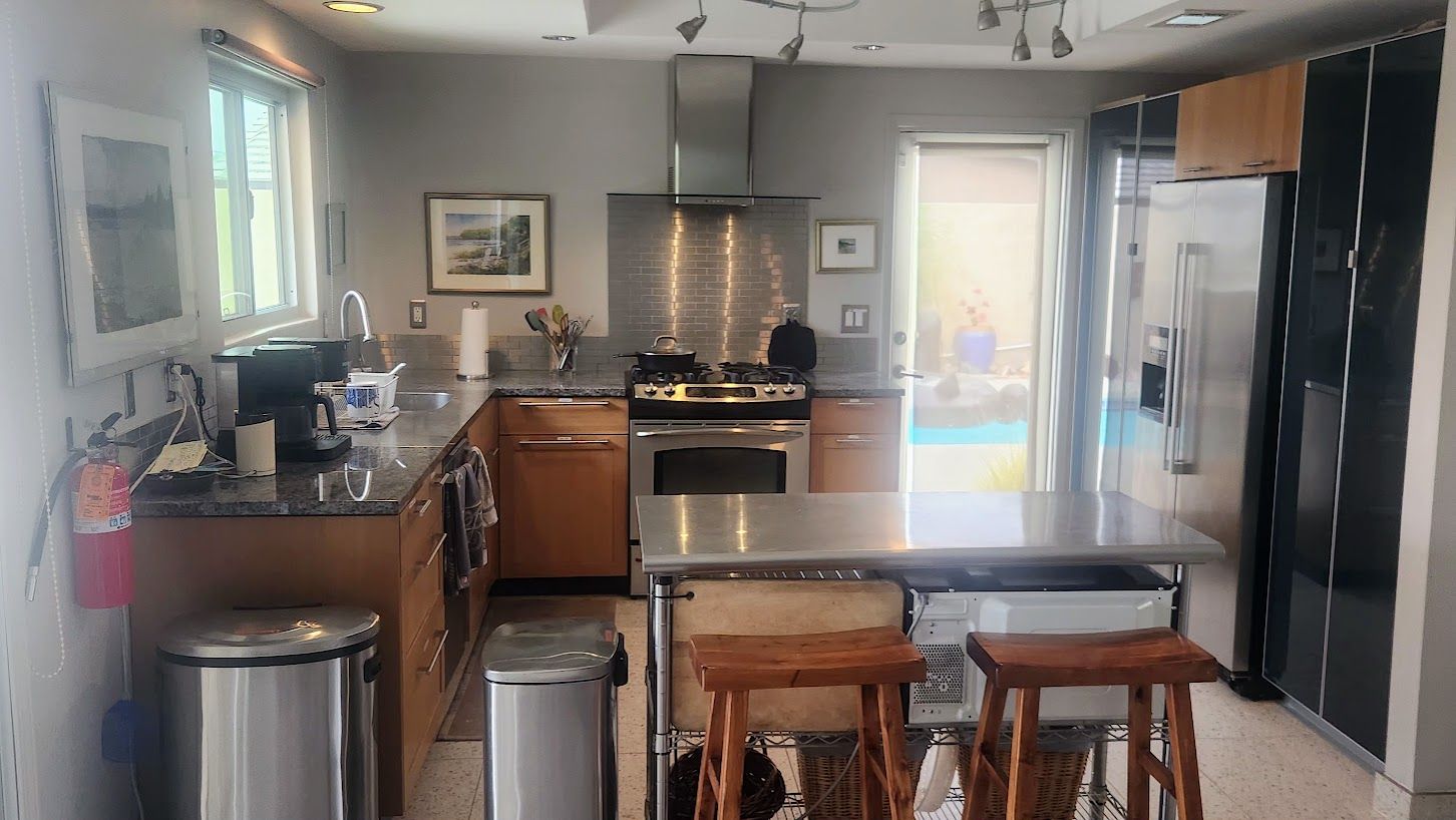 A modern kitchen with stainless steel appliances, wooden bar stools, and a view of a balcony.