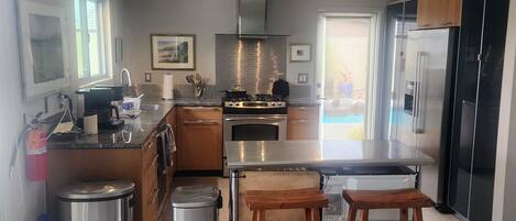 A modern kitchen with stainless steel appliances, wooden bar stools, and a view of a balcony.
