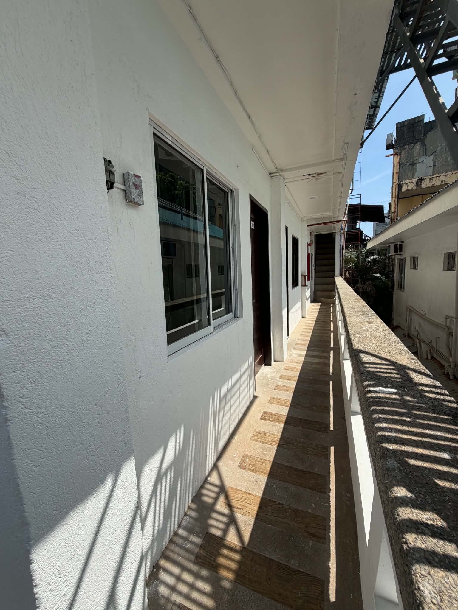 Un pasillo con paredes blancas, ventanas amplias y suelo de madera.