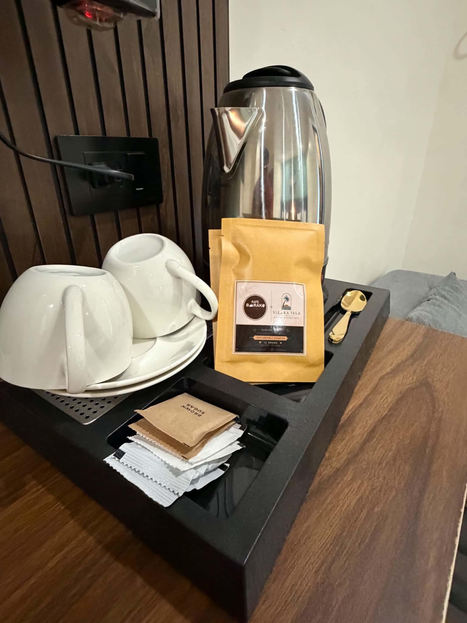 Un coin café comprenant une cafetière, des tasses, un sachet de sucre et une cuillère, le tout disposé sur un plateau.