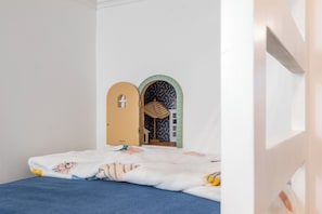 A child's bedroom with a bed, a small play area, and a door leading to another room. - Heron's Hideaway / Ocean View, Steps to the Beach (Hilton Head Island)