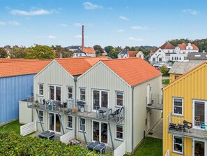 Un immeuble résidentiel avec un toit recouvert de tuiles rouges, un balcon agrémenté de mobilier d’extérieur et un garage.