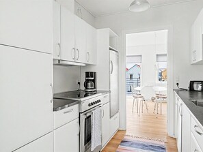 A modern kitchen with white cabinetry, a stove, and a coffee maker. There is a dining area with a table and chairs visible through an open door. - "Leefke" - 200m from the sea by Interhome (Rudkøbing)