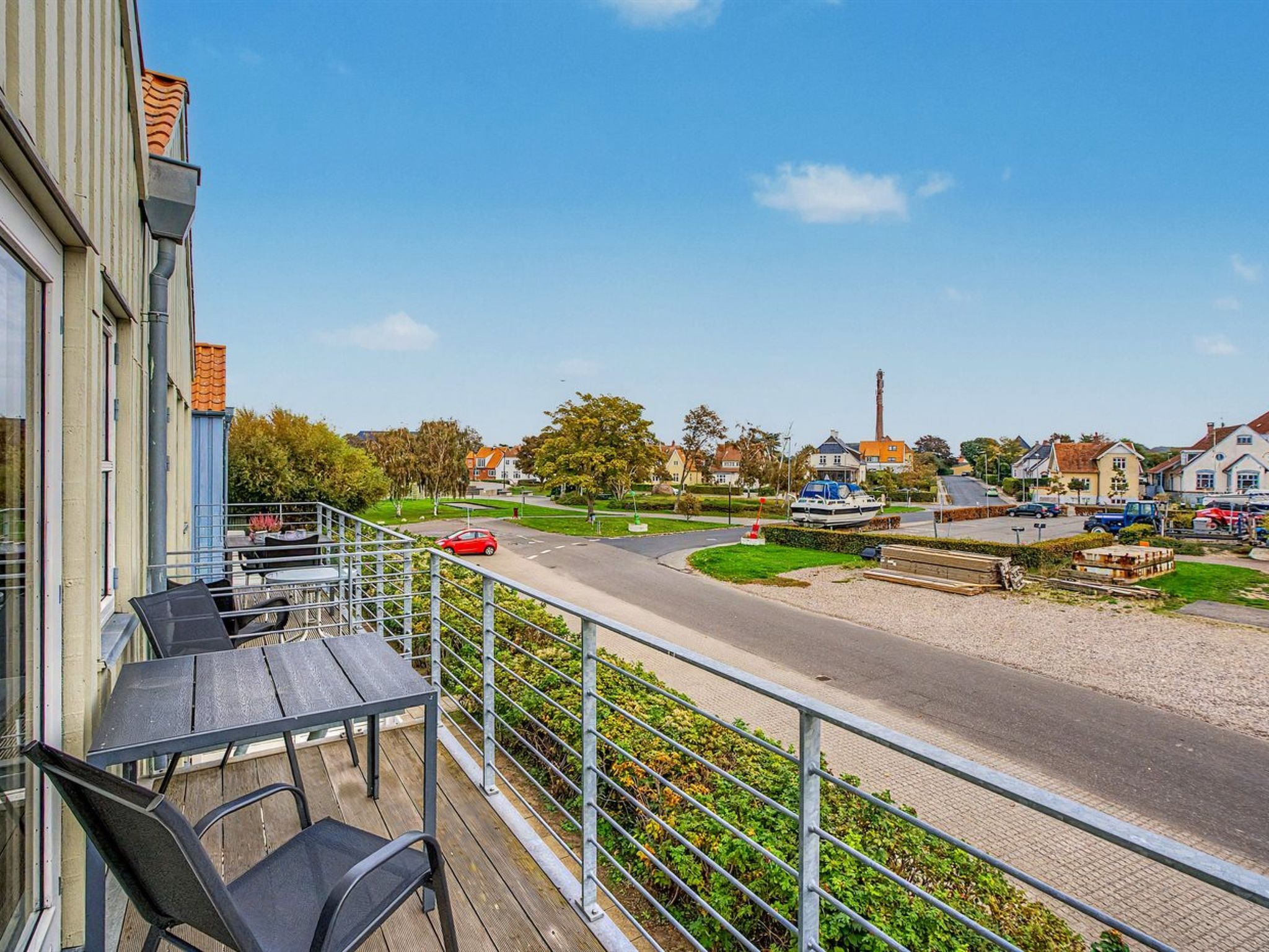 A balcony with outdoor furniture, a clear view of a road, and residential buildings in the background.