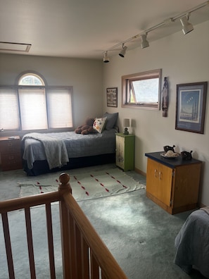 Une chambre à coucher comprenant un lit, une commode, une table de chevet et une fenêtre avec des stores.