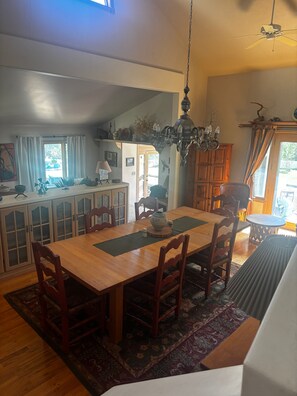 Un espace repas comprenant une table en bois, des chaises, un lustre et une vue sur l’extérieur.