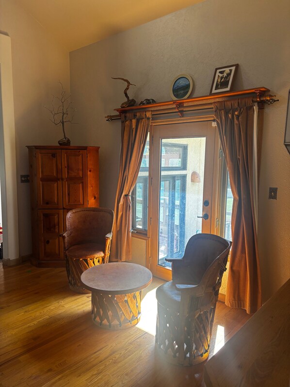 Une pièce avec un plancher en bois, une armoire en bois, deux chaises, une table et une vue sur l’extérieur, visible à travers une porte.