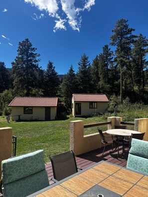 Un espace patio avec une table et des chaises, deux bâtiments aux toits recouverts de tuiles rouges et un paysage boisé en arrière-plan.