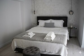 A neatly made bed with white linens and a grey throw, a small bedside table with a lamp, and a wall-mounted light fixture. - OCEANIVES LUXURY VILA IN PALIO KAVALA ME KΗΠΟ (KAVALA)