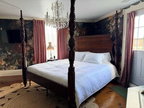 A bedroom with a four-poster bed, a chandelier, and floral wallpaper.