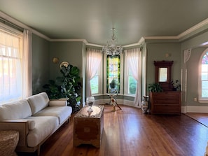 A room with a wooden floor, a white sofa, a wooden chest of drawers, and a large plant.
