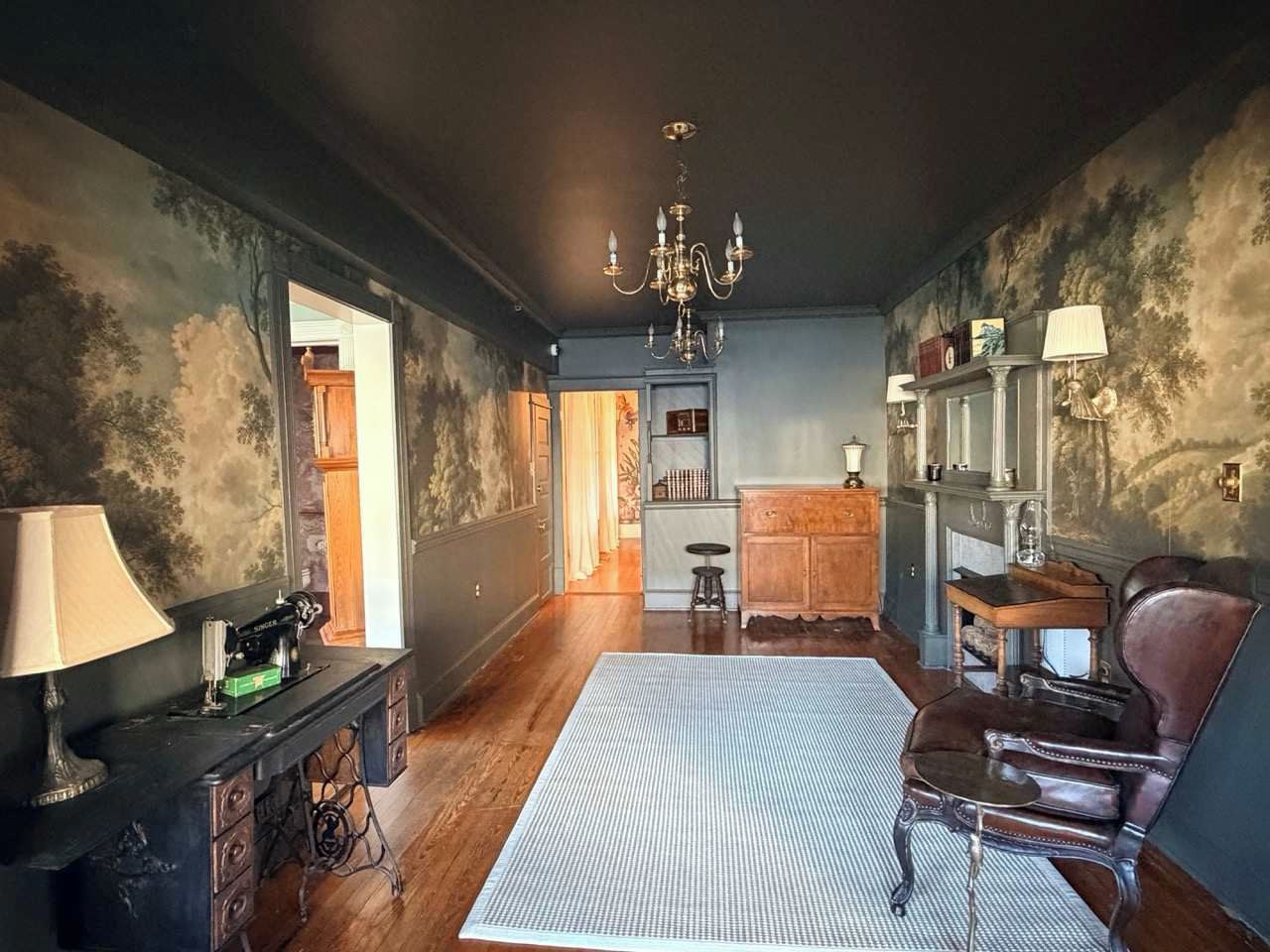 Une pièce avec un lustre, une machine à coudre ancienne, un meuble en bois et un fauteuil en cuir.