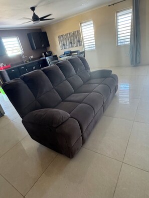 A living room with a sectional sofa, a ceiling fan, and a kitchen area in the background. - ZEMMA Apartments Unit 3 (Willemstad)
