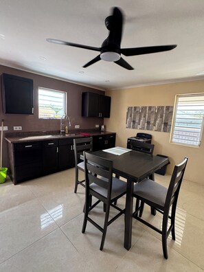 A modern kitchen with a dining area, featuring a ceiling fan, dark cabinetry, and a tiled floor. - ZEMMA Apartments Unit 3 (Willemstad)