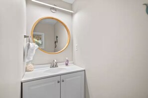 Un baño con un espejo redondo, un lavamanos y un perchero para toallas.