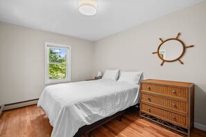 Un dormitorio con cama, cómoda, ventana y un objeto circular fijado a la pared.