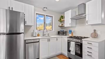 A modern kitchen with white cabinets, stainless steel appliances, and a window with a view of trees.