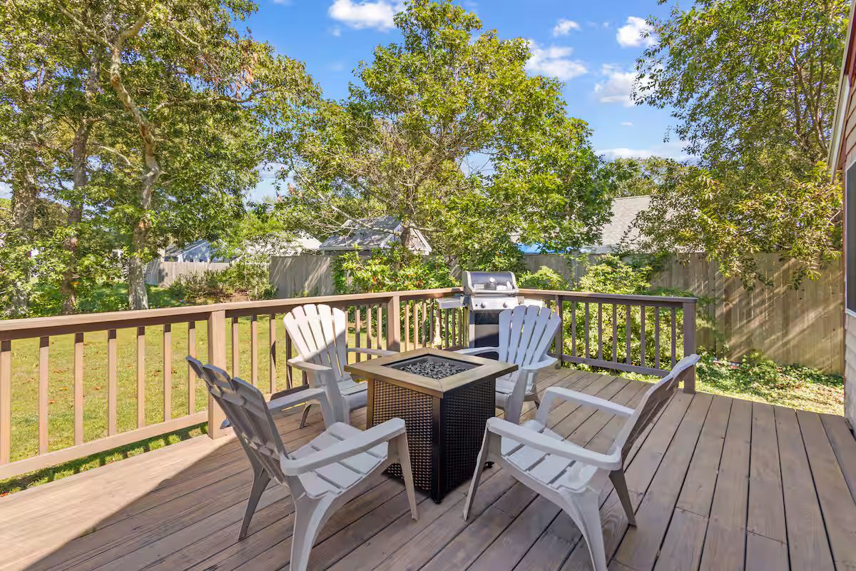 Een terras met een barbecue, een vuurkuil en vier Adirondack-stoelen.