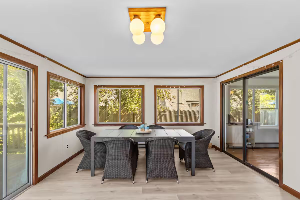 A dining area with a table and chairs, large windows, and a view of the outdoors.