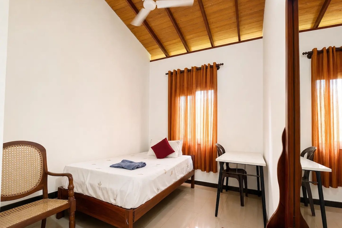 A room with a bed, a desk, a chair, and a ceiling fan.