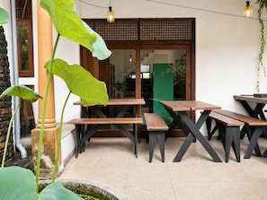 Un espacio al aire libre con mesas y bancos de madera, un pilar de piedra y una puerta verde.