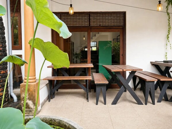 An outdoor seating area with wooden tables and benches, a stone pillar, and a green door.