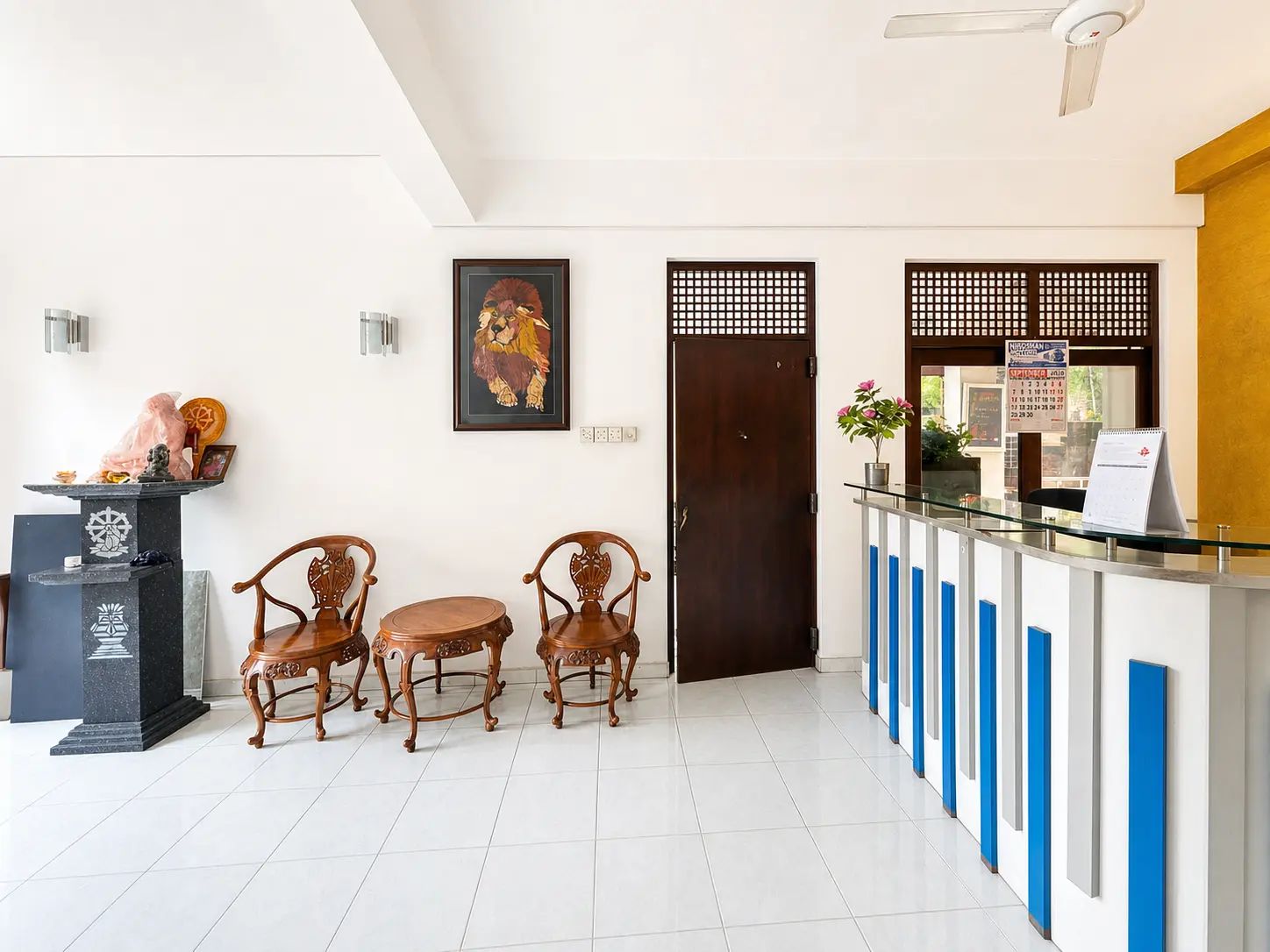 A reception area with a reception desk, a wooden chair, a framed artwork, and a door.