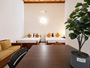 A room with two beds, a wooden table, a sofa, and a potted plant.