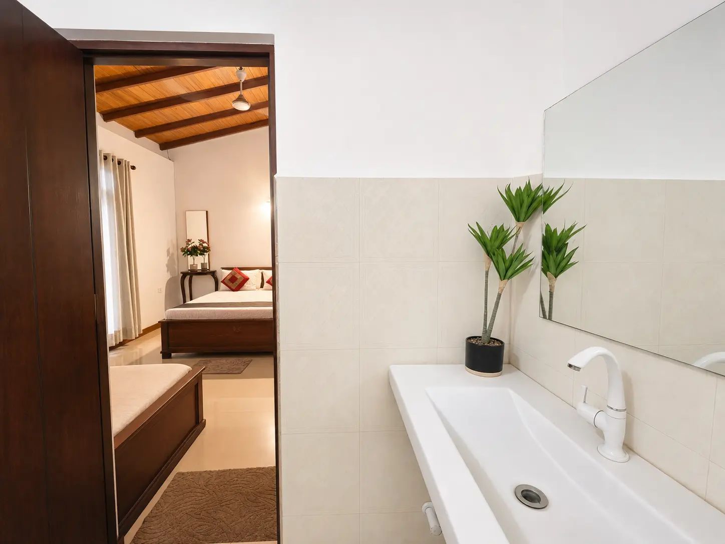 Um banheiro moderno com pia branca, um espelho e duas plantas em vasos.
