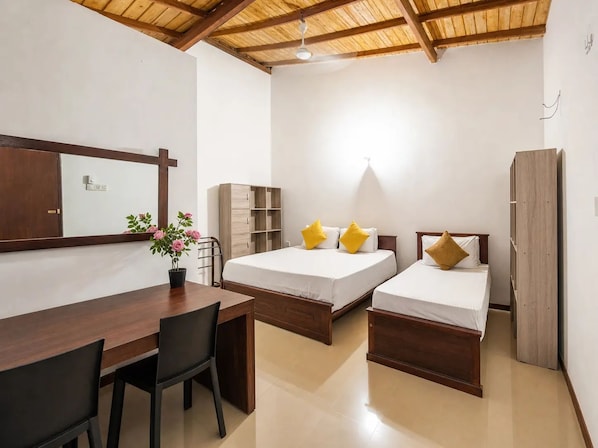 A room with two beds, a desk, a chair, a wardrobe, and a potted plant.