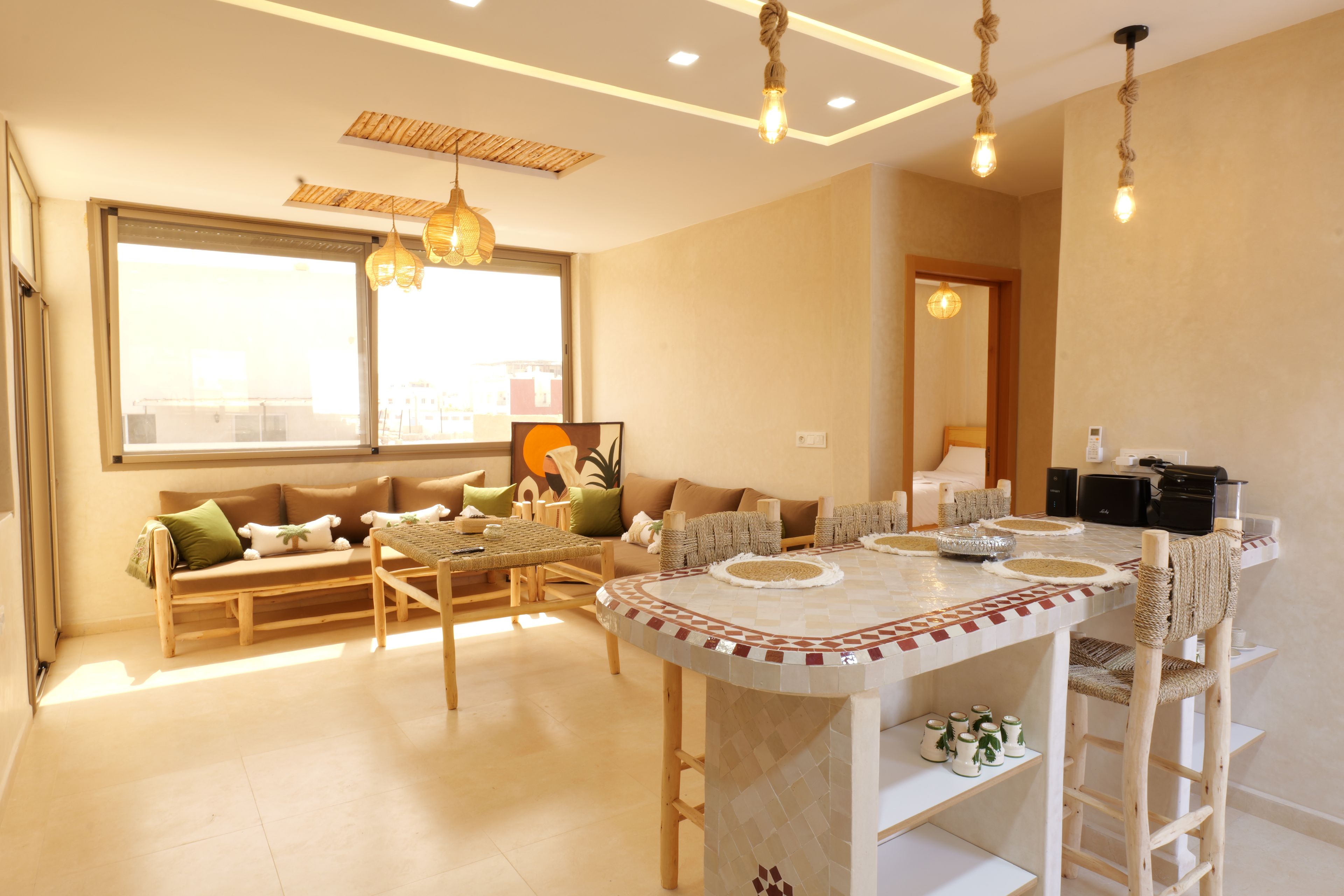 A modern living room with a large window, a dining area with a round table, and a seating arrangement.