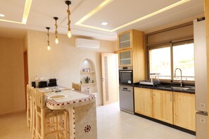 A modern kitchen with wooden cabinets, a built-in oven, and a large window. - Authentic Apartment in Tamraght – A Peaceful Stay Near the Beach (Tamraght)