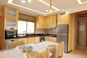 A modern kitchen with wooden cabinets, stainless steel appliances, and a central island with woven chairs. - Authentic Apartment in Tamraght – A Peaceful Stay Near the Beach (Tamraght)