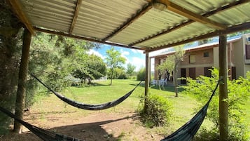 Una hamaca bajo techo metálico, un patio con césped y un edificio con ventanas.