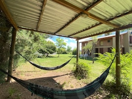 A hammock under a metal roof, a grassy yard, and a building with windows.