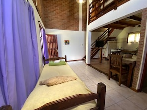 A room with a bed, a dining table, and a staircase leading to an upper level.