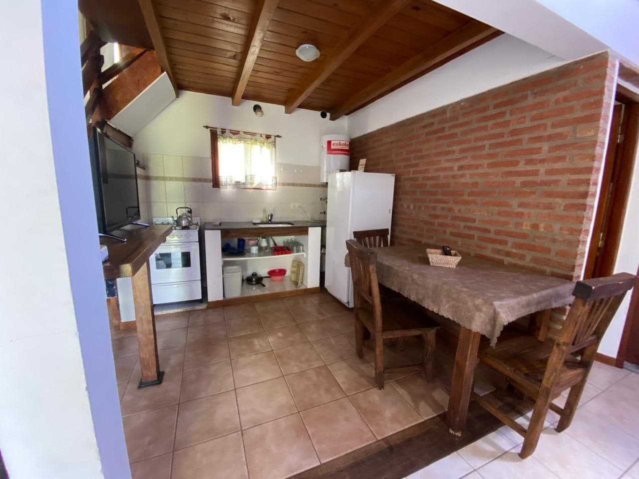 A kitchen with a brick wall, wooden ceiling, and a dining area with a table and chairs.