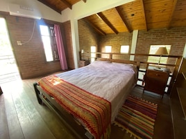 A bedroom with a wooden bed, a brick wall, and a sloped ceiling.