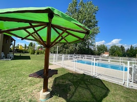 A pool area with a fenced pool, a green umbrella, and a wooden bench.