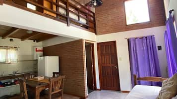 Een ruime kamer met een hoge plafond, een balkon, een eethoek met houten meubels, en uitzicht op een keuken.