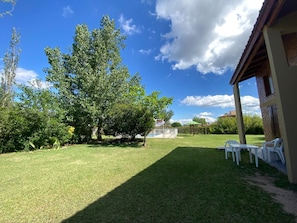 A backyard with a pool, a covered patio area, and a large tree.